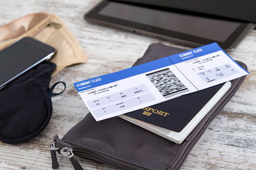 A tablet, phone, passport, airplane ticket, and other travel supplies sit on a wooden table.