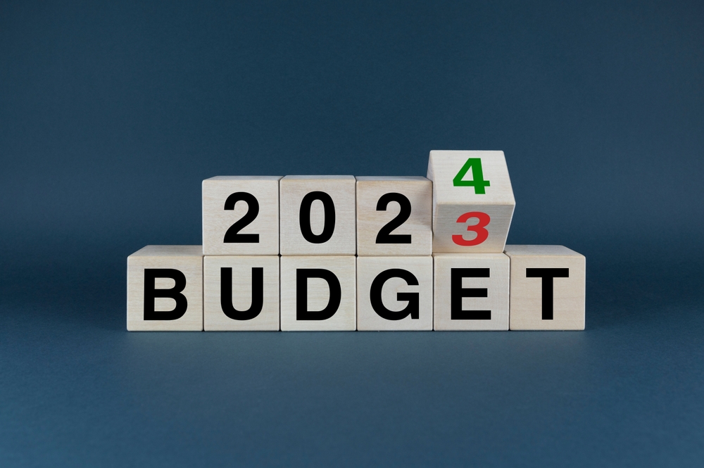 Wooden blocks on a blue background that spell out 2024 BUDGET. The final block is rotating to change from 3 to 4.