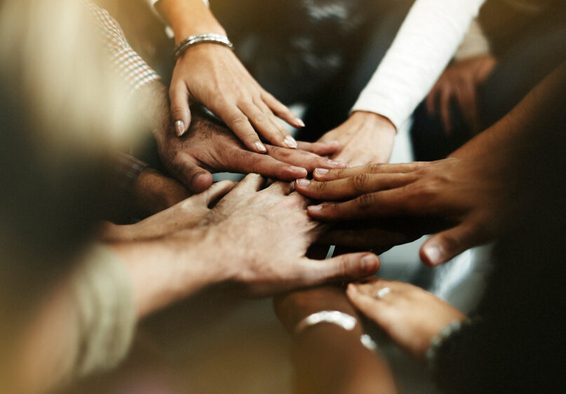 A diverse group of teammates hold out their hands and join them to show unity.