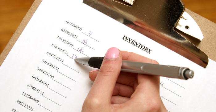 A person writing quantities on an inventory sheet with a list of serial or item numbers.