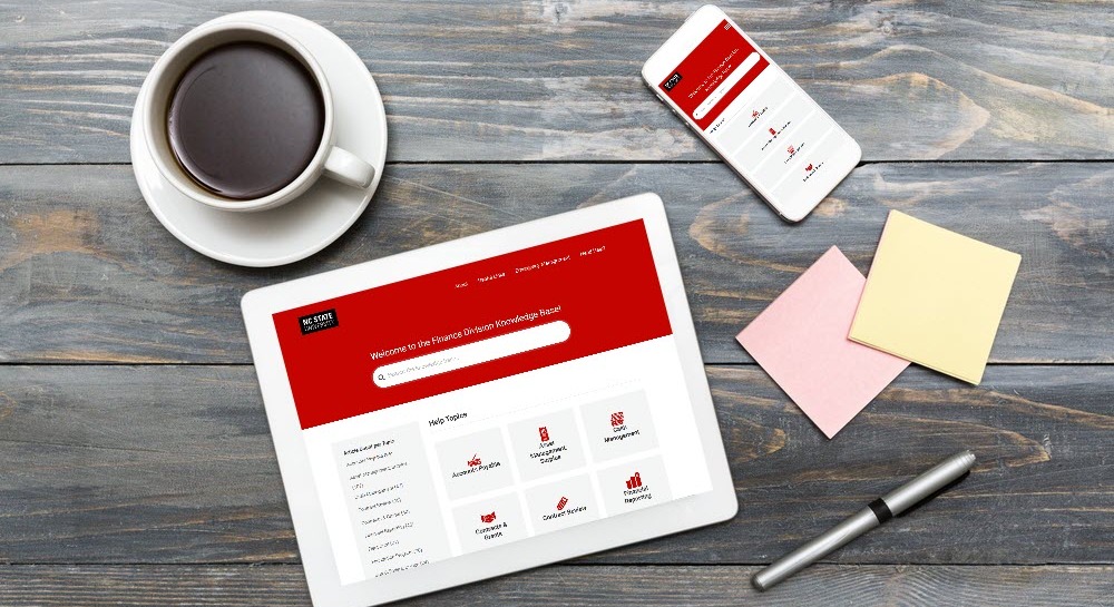 A cup of coffee, sticky notes, pen, cell phone and tablet on a wooden table. The cell phone and tablet have the Finance Division Knowledge Base open.