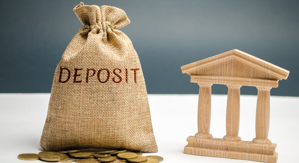 A burlap sack labeled "DEPOSIT" sits next to a wooden toy bank and gold coins.
