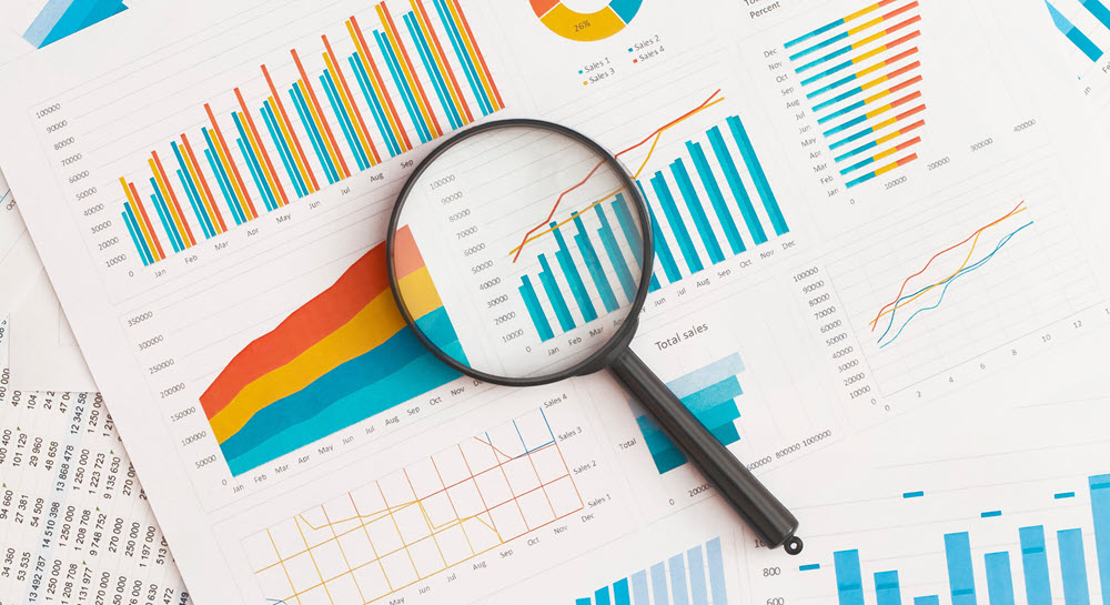 A magnifying glass resting on top of a table covered in printouts of charts and graphs