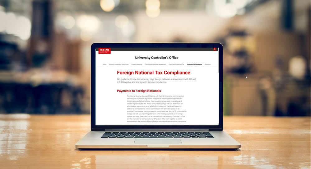 A laptop sitting on a desk. The laptop has the University Controller's Office website article on Foreign National Tax Compliance open.