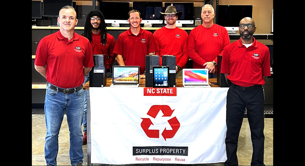 The Materials Support team posing in the Restore with a selection of refurbished devices for sale