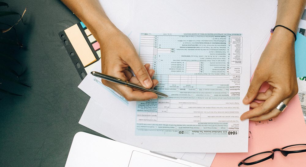A person completing an IRS form 1040 at a desk that is covered in other papers