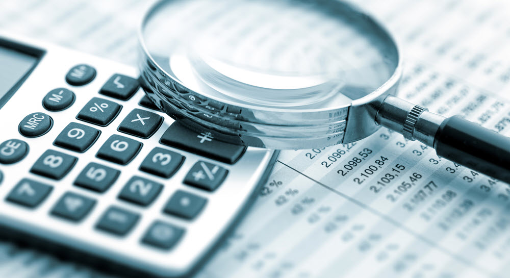 A magnifying glass and calculator sitting on top of a financial spreadsheet