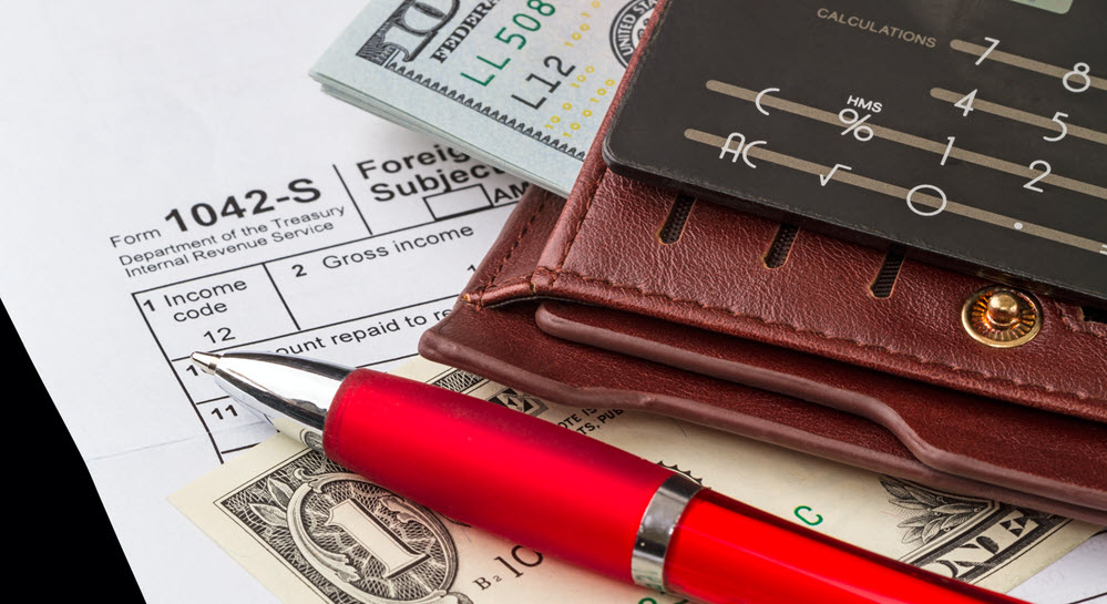 A pen, cash, a wallet, and a calculator sitting on top of an IRS tax form