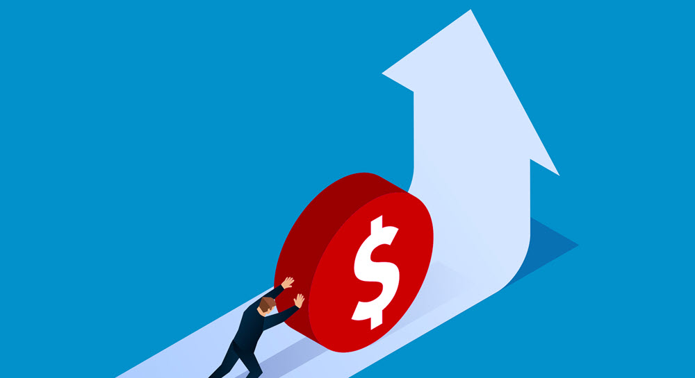 A man rolling a red disc witha dollar sign on it up an incline that is shaped like an upward arrow