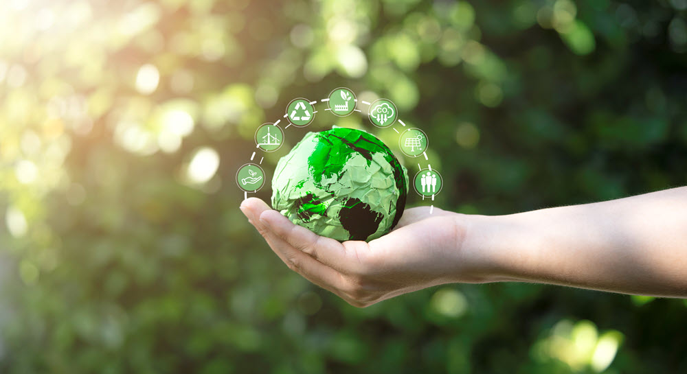 A hand holding a green, ball-sized model of Earth with recycling and sustainability icons above it