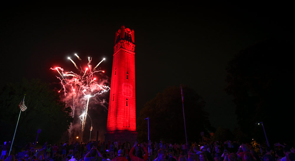 The belltower lit up in red with fireworks exploding nearby