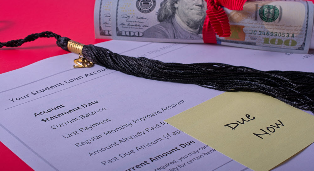 A student loan account billing statement labeled "Due Now" with a tassle and gift money resting on top