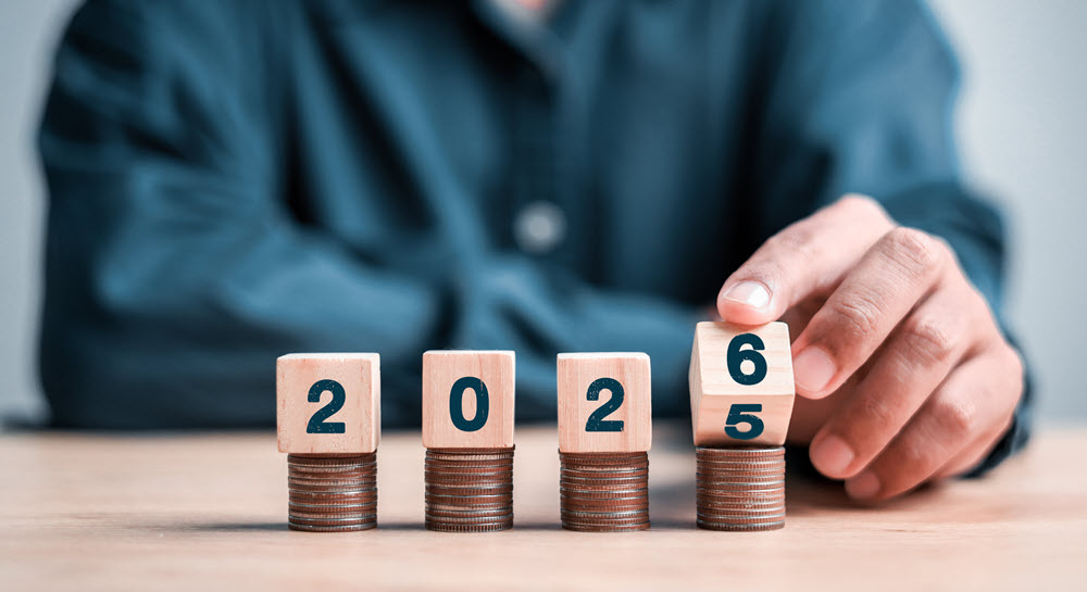 Wooden blocks labeled 2025 stacked on coins. The 5 block is turning over to reveal the number 6, so the year is becoming 2026.